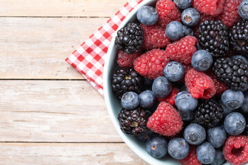 Fresh assortment berries in bowl on wooden table. Top view. Copy space