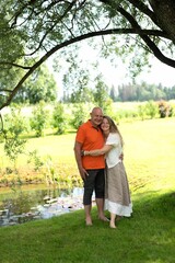 Naklejka premium Daughter hugging her father under a tree in a sunny park with a pond in the background