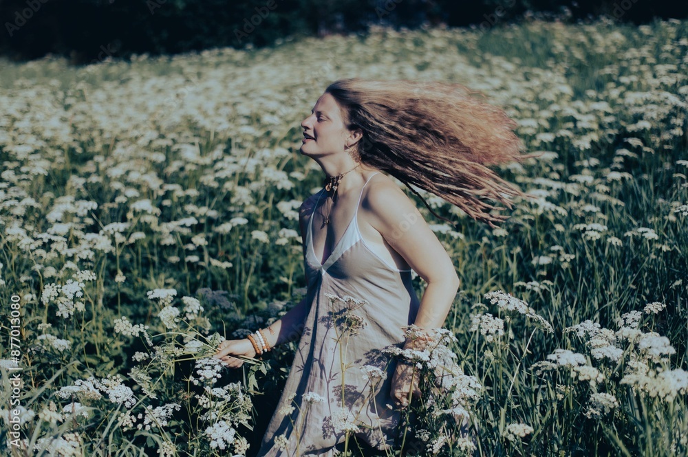 Wall mural young woman posing in a field of white wildflowers on a sunny day