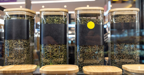 Tea of different varieties in glass jars stand in a row on a store shelf. Label with place for text.