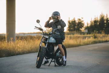 Naklejka premium A biker puts on a helmet while sitting on a motorcycle..A man rides a motorcycle at sunset.