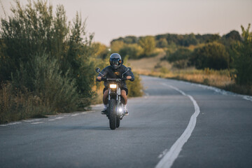 A biker rides his cafe racer motorcycle at sunset.