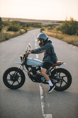 Fototapeta premium Biker on a cafe racer motorcycle on the road at sunset. Concept of riding a motorcycle at sunset.
