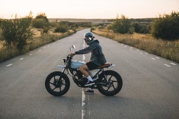 Biker on a cafe racer motorcycle on the road at sunset. Concept of riding a motorcycle at sunset.