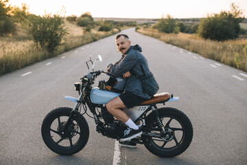 Young smiling man on a motorcycle on the road at sunset. Concept of riding a motorcycle at sunset.