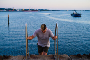 Front view of young man climbing stairs to the port with a boat and the sea in the background