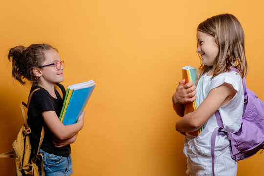 Two schoolgirls laughing and holding books on yellow backdrop