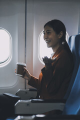 Smiling Asian woman enjoying smartphone comfortable flight while sitting in the airplane cabin, Passengers near the window.