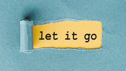 A yellow piece of paper with the phrase Let It Go written on it has been torn from a blue sheet of paper, leaving a jagged edge.