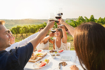 Happy adult friends having fun drinking red wine and eating together with vineyard in background -...