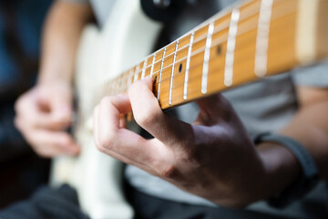 Close up of a man’s left hand and finger on natural brown wooden neck of white electric guitar...
