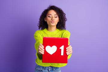 Photo of young wavy haired kissing girl in green pullover holding red like button dating network isolated on violet color background