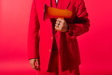 Handsome young Indian man in red suit holding a megaphone.