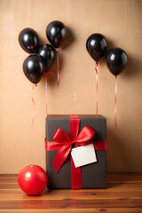Black gift boxes with red ribbons and floating black and red balloons are standing against a brown background with a blank black sign for your text
