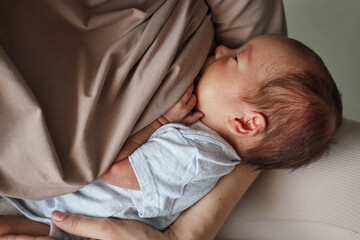 Unrecognizable mother wearing beige clothing breastfeeding newborn baby while sitting indoor...