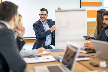 Business man pointing to the whiteboard showing diagram and smiling while talking to his colleagues during conference presentation.