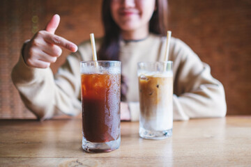 Closeup image of a young woman pointing finger at two glasses of iced coffee