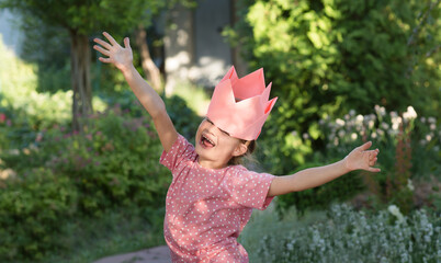 A portrait child girl  with paper crown having fun and dance at a children's party in a summer...