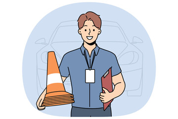 Man instructor from driving school smiles and holds traffic cones inviting to take exam for driver license. Guy employee of car school advertises services company teaching driving.