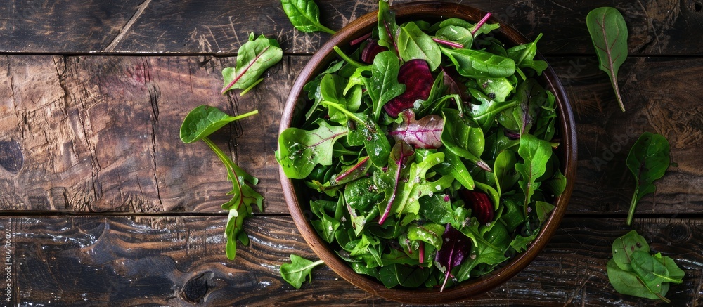 Poster a bowl of fresh green salad featuring spinach, arugula, and beetroot leaves on a rustic wooden surfa
