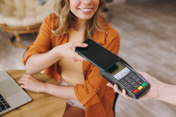 Close up young woman hold bank payment terminal to process acquire mobile cell phone pay bill sits...