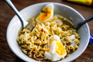 Boiled noodles with pieces of egg isolated in a white bowl on a wooden table.