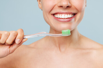 Close up cropped smiling happy half naked topless young woman with nude make up brushing teeth isolated on plain blue color background. Skin care healthcare hygiene cosmetic oral procedures concept.