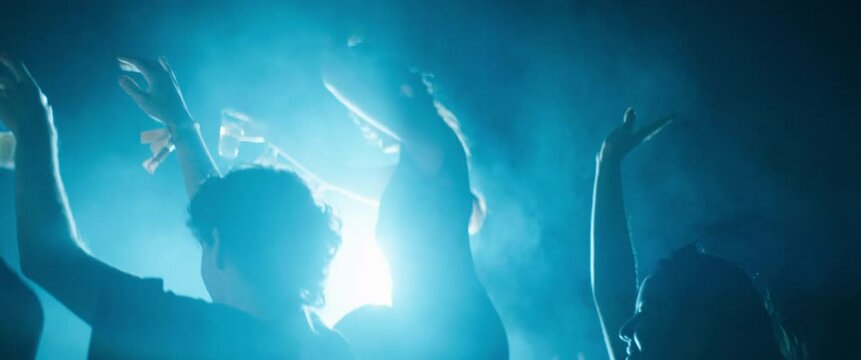 A young woman dances on her friend's shoulders as they enjoy the music at a festival at night. Captured using an anamorphic lens and presented in the 2.39:1 CinemaScope aspect ratio.