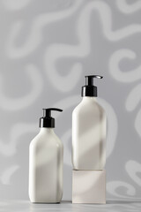 Two white dispensers with cosmetics with a place for the logo on a grey background with shadows.