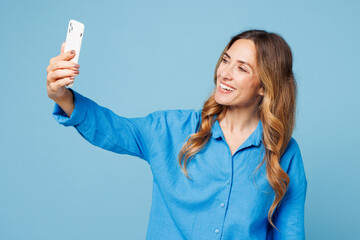 Young woman she wears shirt casual clothes doing selfie shot on mobile cell phone post photo on social network isolated on plain pastel light blue cyan background studio portrait. Lifestyle concept.