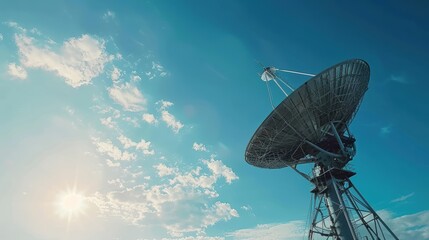 A large satellite dish antenna against a clear blue sky with scattered clouds, capturing signals for communication and broadcasting purposes.
