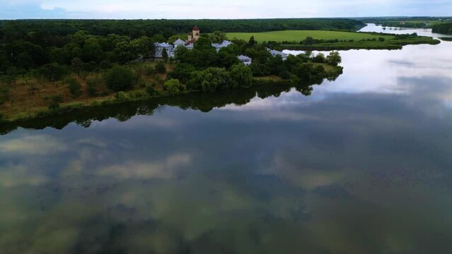 High angle drone footage of Manastirea Caldarusani and it's surrounding lake on a warm summer day. Calm water around a forrest in which a monastery is situated. Aerial shot christian of temple.
