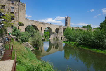 Obraz premium Girona, Spain - 7 July, 2024: Reflections of the medieval Pont Vell bridge on the River Fluvia at Besalu, Catalonia