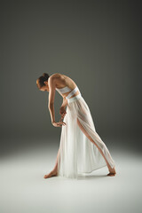 Young ballerina in white dress gracefully bends over while dancing.