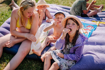 limbazi, Latvia, June 29, 2024 - Children sitting on an air mattress at a campsite, enjoying snacks and a sunny day, with tents and greenery in the background...