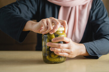 A woman tries to open a jar of pickles with all her strength