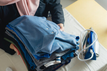 woman picking up stack of clothes that has finished ironed and folded, finished housework