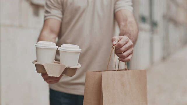 Unrecognizable Close-up of a delivery man holding takeout coffee and a brown paper bag, providing quick and efficient service.