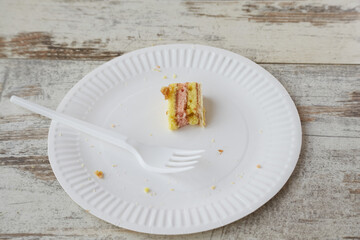 Uneaten piece of layered sponge cake on white plate with fork on wooden table, last piece of fruit...