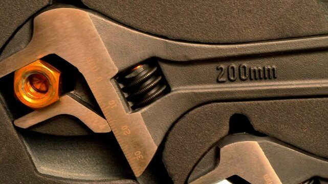 Closeup of three different sized adjustable wrenches in a fitted case, each holding a steel nut in the open jaws.