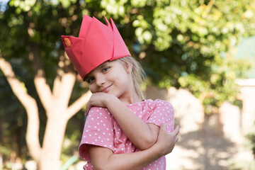 A portrait laughing child girl  looking at the camera with paper crown having fun and dance at a children's party in a summer garden. children's birthday.
