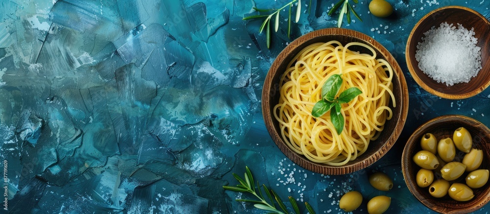 Poster an italian plate of anchovy spaghetti with salt in a wooden bowl and olives on a blue texture backgr