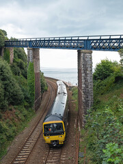 A local passenger train passing under the East Cliff bridge on the approach to Teignmouth station in Devon, UK. This stretch of track forms part of the spectacular route along the coastline