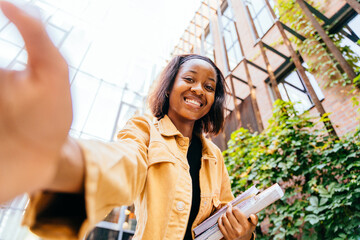 A young woman wearing a yellow jacket is smiling and holding a stack of books. Concept of happiness and accomplishment, as the woman is proud of her studies or her current situation