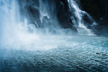 Naklejka premium Moody waterfall flowing in tropical rainforest at Milford Sound