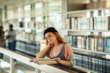 Young female student reading in busy college library