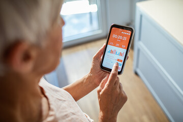 Rear view of a middle aged woman tracking workout time on smartphone