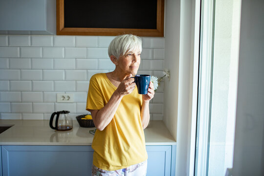 Middle aged woman holding cup of coffee looking out window at home