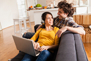 Joyful couple using laptop together on sofa in modern home interior