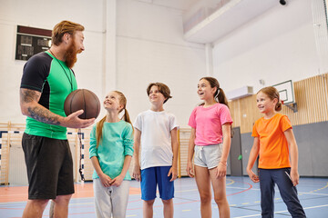 A man holds a basketball, leading a diverse group of kids in a vibrant classroom setting.